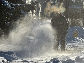 A man works at blowing the packed down snow off the sidewalk as the sunlight makes the snow sparkle in south Edmonton, Dec. 17, 2021.