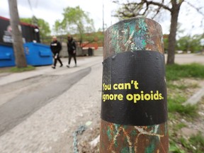 Pedestrians make their way past a sticker raising awareness about opioids in an alley near 81 Avenue and Calgary Trail, in Edmonton Friday May 28, 2021.