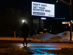 A pedestrian crosses 104 Avenue at MacEwan University while a government advertisement calling for COVID-19 booster shots to combat the Omicron strain outbreak is shines in the background in Edmonton, on Wednesday, Jan. 12, 2022. Photo by Ian Kucerak