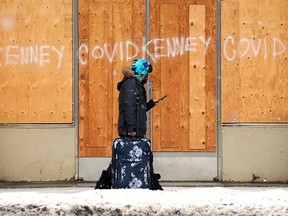 A person carries luggage past Jason Kenney and COVID-19 graffiti on a long boarded up building near 103 Avenue and 106 Street, in Edmonton on Wednesday, Jan. 26, 2022. Photo by David Bloom
