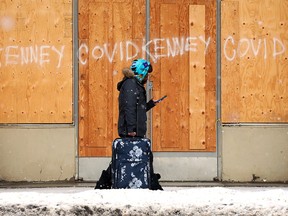 A person carries luggage past Jason Kenney and COVID-19 graffiti on a long boarded up building near 103 Avenue and 106 Street, in Edmonton on Wednesday, Jan. 26, 2022.