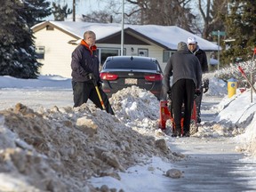Neighbours Dana Sydor, Isa  Khurshed, and Nizam Khurshed clear the windrows from in font of their homes shortly after a grader had created them on Wednesday, Jan. 12, 2022 in north Edmonton.