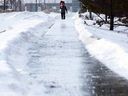 Um pedestre caminha por uma calçada gelada enquanto carrega cones de trânsito em uma colisão de dois veículos, em Edmonton, na segunda-feira, 17 de janeiro de 2022. 