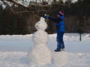 Henry Corcoran, 7, putting on a hat for the snowman he built with his parents at Hawrelak Park in Edmonton, January 11, 2022. Ed Kaiser / Postmedia