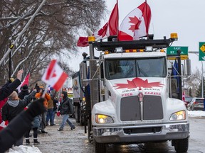 Truck convoy cheered by people on downtown Edmonton street.