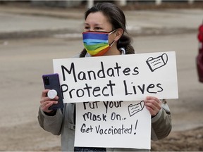 A lone pro-vaccine mandate protester carries a sign as people protesting COVID-19 health measures begin to gather at the Alberta Legislature in Edmonton on Saturday Feb. 12, 2022.