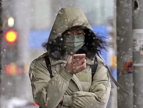 A woman checks her phone in downtown Edmonton on Monday March 7, 2022 amid snow flurries and wind gusts of 40 km/hour. (PHOTO BY LARRY WONG/POSTMEDIA)