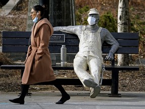 A woman walks past a statue wearing a face mask in Edmonton during the COVID-19 pandemic on April 14, 2021.