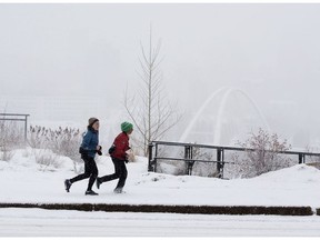The Edmonton skyline is obscured by blowing snow as joggers, one of whom is Alberta NDP Leader Rachel Notley, left, make their way along Saskatchewan Drive in Edmonton on Sunday, March 20, 2022.