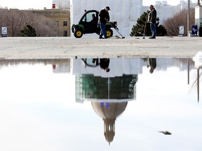 Crews are reflected in a puddle as they work to clear away dirt and gravel put down over the winter in Violet King Henry Plaza, at the Alberta Legislative grounds in Edmonton, Thursday March 31, 2022.