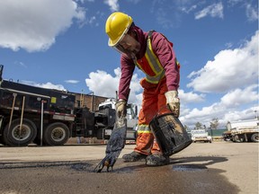 Brandon Auger, with the City of Edmonton, brushes tar around a pothole as it is prepared to be filled with asphalt  on Thursday, April 28, 2022.