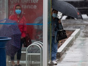Transit riders wait for their bus as the rain falls near 109 Street and Jasper Avenue in downtown Edmonton, on Thursday, May 19, 2022. Rainstorms moved through the city all day.