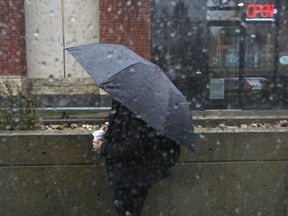 A pedestrian with an umbrella and a coffee walks near 109 Street and Jasper Avenue during a downpour in downtown Edmonton, on Thursday, May 19, 2022. Rainstorms moved through the city all day.