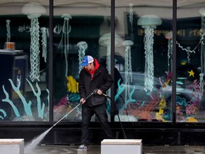 Jayden Quinn power washes the sidewalk in front of an
underwater scene in the Southpark On Whyte building,10615 82 Ave. in Edmonton, Monday May 9, 2022. The art installation is a collaboration between Southpark On Whyte, Vignettes, and ECKZ studioz. Photo By David Bloom