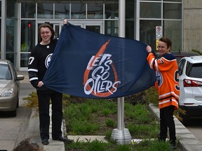 MacEwan University president and vice-chancellor Dr. Annette Trimbee, right, and Myles Dykes, president of the students' association, hold an Oilers banner on Wednesday, May 18, 2022, at MacEwan University after raising a Oilers flag on the pole as they enter a friendly wager with Mount Royal University in Calgary on the result of the Battle of Alberta playoff series. Both universities will be fundraising during the series to donate to their student food banks.