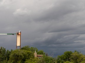 A worker services a dish on the top of a tower at Concordia University while a thunderstorm forms in the distance in Edmonton on June. 22, 2022.