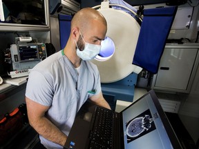 Medical radiologic technologist Jeremy Hayes looks at a CT scan as he poses for a photo at the University of Alberta Hospital Stroke Ambulance, in Edmonton, Friday, June 10, 2022. The ambulances aboard the CT scanner are visible behind Hayes.