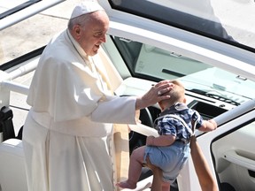 Pope Francis blesses a child as he arrives for an open-air mass at Commonwealth Stadium in Edmonton, Canada, on July 26, 2022. - The Pope with be celebrating the feast of St. Anne, grandmother of Jesus, a day of particular reverence for Indigenous Catholics.