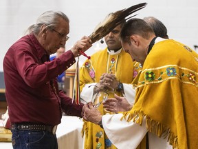 Elder Fernie Marty performs smudging on Father Mark Blom during Mass at the Sacred Heart School gym in Edmonton Alberta, July 10, 2022. Jason Franson for Postmedia