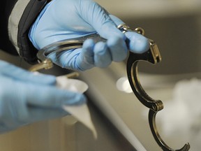 An officer wipes down a pair of handcuffs in the Edmonton Police holding cells. An officer was docked 40 hours of pay last year for failing to help colleagues shackle a resisting prisoner. Details of the decision were released months after the fact due to staffing issues in the EPS FOIPP department.