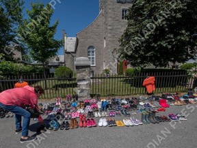 A woman places a pair of children's shoes in front of the St. Francis Xavier Church in Kahnawake, Quebec on Saturday, May 29, 2021, as a memorial to the 215 children whose remains have been found buried at the site of a former residential school in Kamloops.