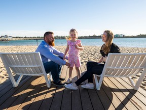 Brian and Sarah Hennessey sit with their daughter Harper, 5, on beach chairs along Jubilation Beach located at Jensen Lakes in St. Albert.