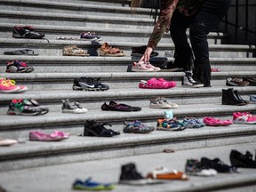 A woman places one of 215 pairs of children's shoes on the steps of the Vancouver Art Gallery as a memorial to the 215 children whose remains are believed to have been found buried at the site of a former residential school in Kamloops, in Vancouver, on Friday, May 28, 2021.