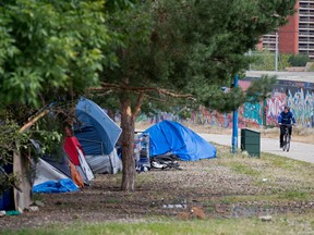 A cyclist makes their way past homeless encampments in Downtown Edmonton on Aug. 5, 2022. An AHS-led task force is looking at what resources are needed to help stop the spread of shigella in inner-city Edmonton since many people don't have reliable access to hygiene facilities.