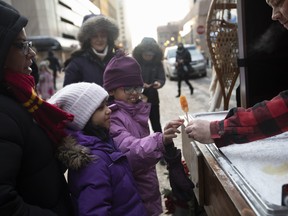 Pranavi Bhatt, 9, gets some maple syrup candy as Meera Bhatt, 7, looks on during the Downtown Holiday Light Up in Edmonton, Alta. on Dec. 3, 2022.