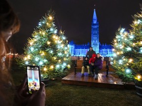 People take photos as the Peace Tower and Centre Block of Parliament Hill are lit with projections for Lights Across Canada in Ottawa on Wednesday, Dec. 7, 2022. Both the House of Commons and Senate have begun a lengthy winter break, but more than a hundred bills are still on the table and ready to be picked up when lawmakers return to Ottawa in late January.