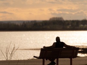 A man rests on a bench as the sun sets over Big Lake at Lois Hole Centennial Provincial Park, across from Lakeshore Estates west of St. Albert, on May 12, 2021.