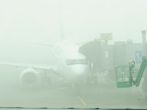 Through the haze of heavy fog, an airplane rests on the tarmac of the Edmonton International Airport on March 23, 2019. The airport recently saw a dozens flight cancellations due to low-lying fog and a U.S. grounding order due to a key aviation system outage.