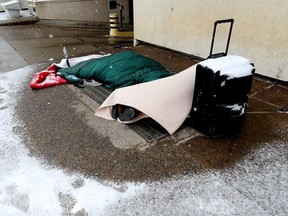 Two people sleep on a warm air exhaust grate outside the Law Courts building in Edmonton on Jan. 27, 2023.