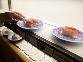 An employee selects a plate of tuna sushi from a conveyor belt at a Kura Corp. sushi restaurant in Kaizuka, Osaka prefecture, Japan Aug. 2017.