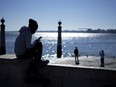 A young man checks his phone by the Tagus river at Lisbon's Comercio square on a sunny winter day, Monday, Jan. 30, 2023.