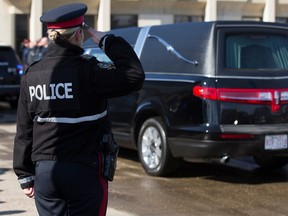 An Edmonton Police Service officer salutes as a procession arrives with the bodies of Const. Travis Jordan and Const. Brett Ryan at the Serenity Funeral Home in Edmonton on Tuesday, March 21, 2023.