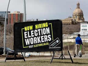 The Alberta legislature is visible behind a sign in Edmonton's river valley on April 26, 2023,  advertising the hiring of election workers ahead of the upcoming Alberta provincial election.
