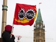 A PSAC worker holds a flag on a picket line in Ottawa, Wednesday, April 19, 2023. Canada's largest federal public-service union and the federal government remain at the bargaining table as workers strike and service disruptions begin to be felt across the country.