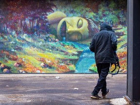 A pedestrian walks past a mural in the Rice Howard Way Alley of Light by Edmonton-based artist Josh Harnack on Thursday, March 30, 2023 in Edmonton.  The murals in the alley depict an examination of humanities dominion over the natural world, its push backs, and monsters.   Greg Southam-Postmedia