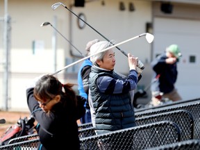 Douglas Tam, centre, practices his golf swing after Edmonton's Victoria Golf Course and Driving Range opened for the season on April 7, 2022.