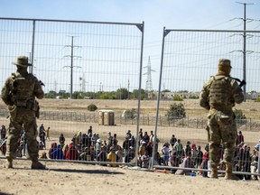 FILE - Migrants wait in line adjacent to the border fence under the watch of the Texas National Guard to enter into El Paso, Texas, Wednesday, May 10, 2023.