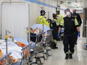 Paramedics transfer patients to the emergency room triage at Toronto's Humber River Hospital during the COVID-19 pandemic, but must leave them in the hallway due to full capacity.
