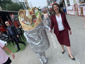 Alberta Premier Danielle Smith walks among the tents at Taste of Edmonton on Thursday, July 20, 2023, accompanied by someone wearing a donair costume similar to the one currently being auctioned by the Alberta government on its surplus auction website.