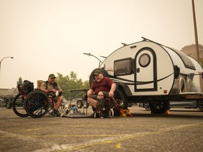 Veteran Rob Pullen, left, and Warren Pullen, who were evacuated from their home on Thursday due to wildfires, sit with their dogs outside their trailer in the parking lot at an evacuation centre, in Kelowna, B.C., on Saturday, Aug. 19, 2023.