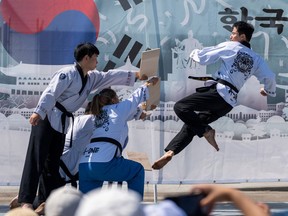 A person wearing a taekwondo outfit leaps into the air to break boards held by three other taekwondo martial artists