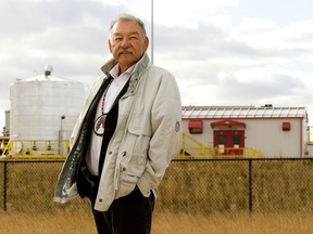 Chief George Arcand Junior poses for a photo in a field with an industrial building in the background