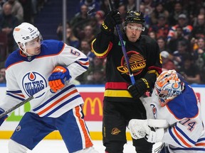 Vancouver Canucks' Andrei Kuzmenko, centre, and Edmonton Oilers' Cody Ceci, left, watch the puck after it deflected off the mask of Edmonton goalie Stuart Skinner during the second period of an NHL hockey game in Vancouver, on Monday, Nov. 6, 2023.