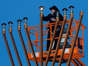 Rabbi Ari Drelich is elevated in a manlift as helights the menorah