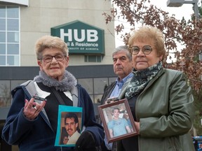 Mike and Dianne Ilesic pose outside with Jane Orydzuk holding photographs of their dead children, with Hub Mall in the background.