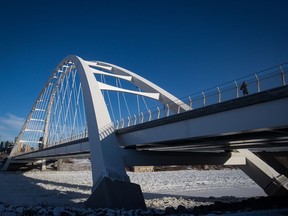 A woman walks across the Walterdale Bridge spanning the ice-covered North Saskatchewan River, in Edmonton, on Friday, Dec. 27, 2019. Alberta's police watchdog is investigating after a man being pursued by officers fell through the river ice in Edmonton and disappeared.